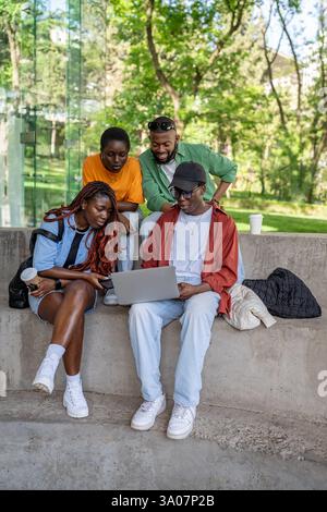 Fröhliche multirassische Gruppen genießen Filme oder Videoanrufe auf dem Laptop draußen. Vier Schüler haben Spaß Stockfoto