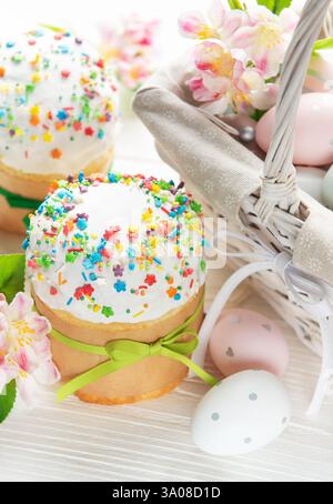 Köstliche osterkuchen mit bunten Streuseln und bemalten Eiern in einem Korb sind von Frühlingsblumen umgeben Stockfoto