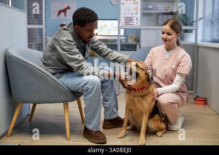 Junge Tierärztin, die Augen eines großen Mischhundes untersucht, der gehorsam auf dem Tisch steht und den männlichen Besitzer in der Tierklinik beobachtet Stockfoto