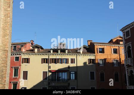 Traditionelle farbenfrohe Wohnhäuser mit Ziegeldächern und Holzläden unter einem klaren blauen Himmel in Venedig, Italien, architektonische Ansicht. Stockfoto