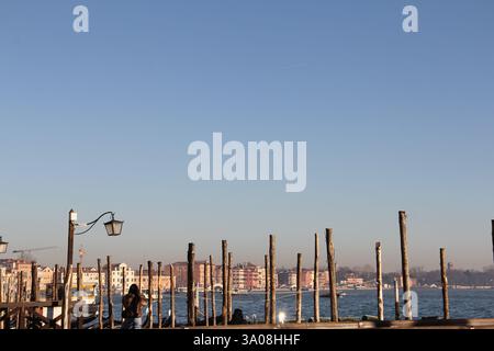 Panoramablick auf die Lagune von Venedig mit traditionellen hölzernen Anlegestellen und farbenfrohen historischen Gebäuden unter einem klaren blauen Himmel in Italien. Stockfoto