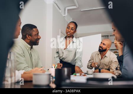 Junge Geschäftsfrau, die männlichen und weiblichen Mitarbeitern im Besprechungsraum im Büro kreative Strategie erklärt Stockfoto