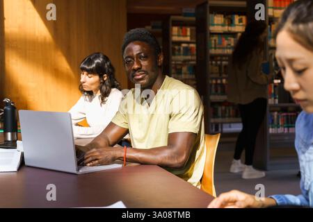 Porträt männlicher Studenten mit Laptop während des Sitzens in der Universitätsbibliothek Stockfoto