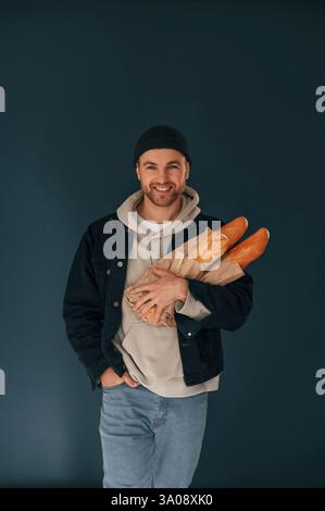 Halten von Baguettes. Ein gutaussehender Mann ist im Studio vor blauem Hintergrund. Stockfoto