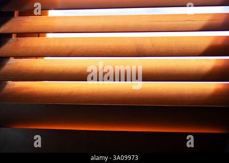 Die warme Sonne scheint hell durch die Fensterjalousien in einem wunderschön beleuchteten Raum und schafft Schatten an den Wänden Stockfoto