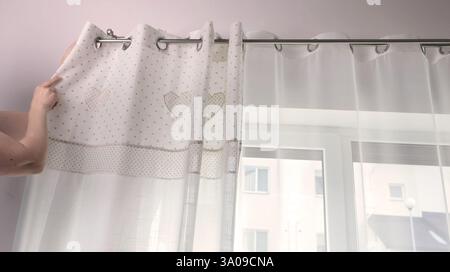 Frau hängt weiße Vorhänge mit Metallringen aus natürlichem Material mit gestickten Herzen in der Küche des Hauses. Reinigung und Sauberkeit. Innenraum Stockfoto