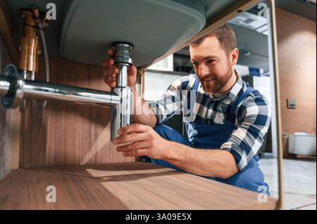Nahansicht. Wasserhahn wird befestigt. Klempner in blauer Uniform arbeitet im Badezimmer. Stockfoto