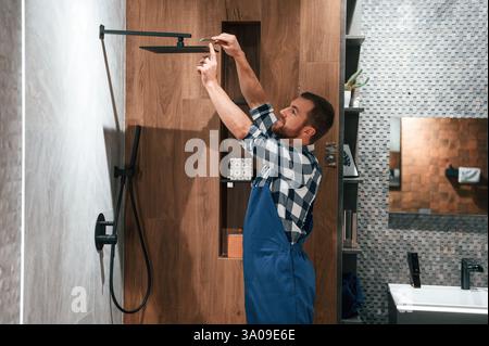 Repariert den Duschhahn. Klempner in blauer Uniform arbeitet im Badezimmer. Stockfoto