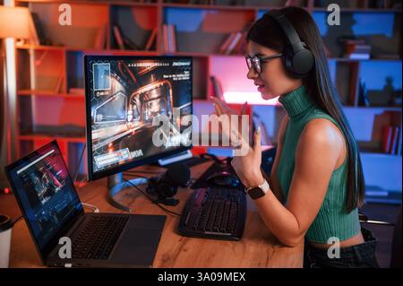 In Kopfhörern. Junge hübsche weibliche Gamerin spielt Shooter. Neonbeleuchtung. Stockfoto