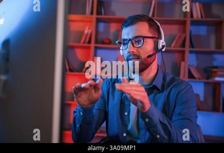 Online-Meetings. Der Mann sitzt zuhause am Computer. Neonbeleuchtung. Stockfoto
