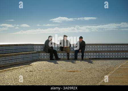 Drei alte Freunde reden an einem sonnigen Tag auf einer Bank Stockfoto