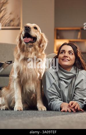 Auf dem Boden liegen. Die Frau ist mit goldenem Retriever-Hund zu Hause. Stockfoto