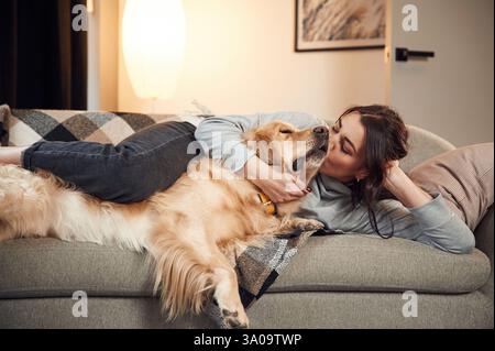Zusammen auf dem Sofa liegen. Die Frau ist mit goldenem Retriever-Hund zu Hause. Stockfoto