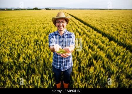 Porträt eines fröhlichen Bauern auf seinem Weizenfeld. Er ist zufrieden mit der Saison und der Ernte in der Hand. Stockfoto