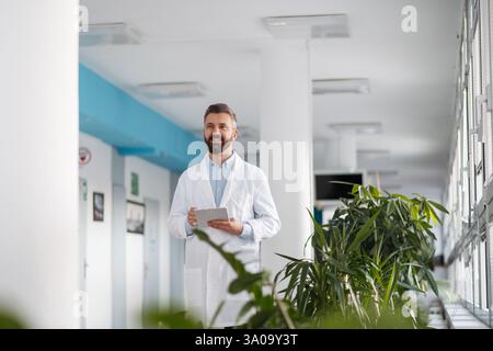 Porträt des Arztes im Krankenhausflur, Tablette mit Krankenakten halten. Stockfoto