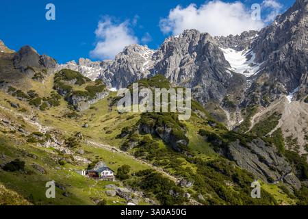 Eine Berghütte auf einem grünen Hügel mit zerklüfteten Gipfeln im Hintergrund. Flaggen werden in der Nähe des Gebäudes angezeigt. Das Huttengebirge refugio in Österreich Stockfoto