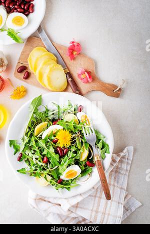 Löwenzahnsalat mit Eiern, Kartoffeln und Bohnen auf hellen Tischhintergrund Stockfoto