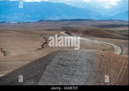 Kurvenreiche, unbefestigte Straße führt durch die karge Landschaft der Agafay-Wüste in Marokko. Stockfoto