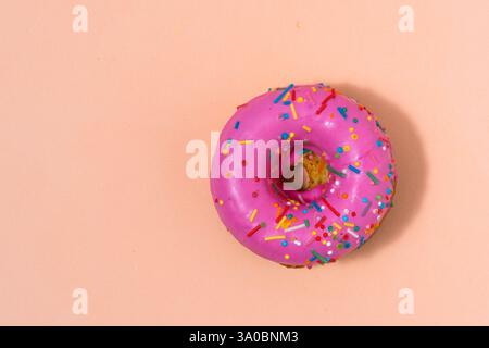 Rosafarbener Donut mit bunten Streuseln auf pastellfarbenem beigem Hintergrund Stockfoto