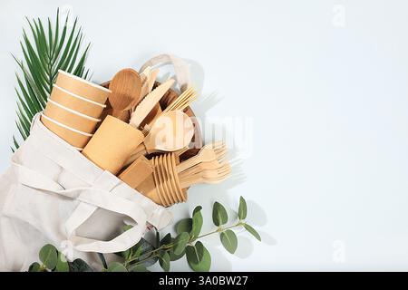 Ein Set umweltfreundlicher Gerichte in einer Öko-Tasche auf einem sonnigen Tisch. Pappbecher, Teller, Kraftpapierservietten, Grillhalme, Holzgabeln, Löffel Stockfoto