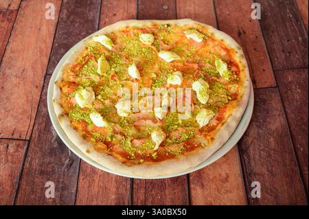 Eine Pizza mit vielen Belägen einschließlich Käse, Schinken und grüner Paprika. Die Pizza steht auf einem Holztisch Stockfoto