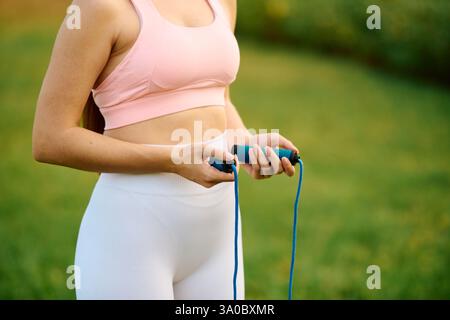 Die aufgeregte junge Frau hält ein Sprungseil, bereit, ihre Outdoor-Fitness-Routine im Park zu beginnen. Stockfoto