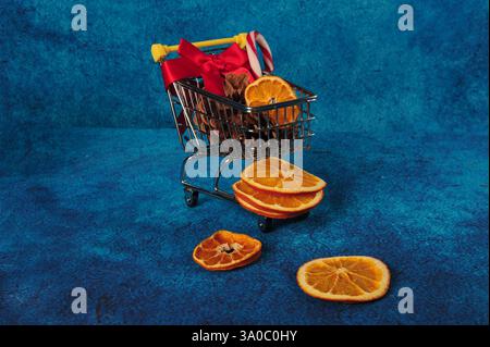 Farbenfrohes Foto des Mini-Einkaufswagens mit roter Schleife und orangefarbenen Scheiben. Orangefarbene Schichten auf der blauen Oberfläche. Stockfoto