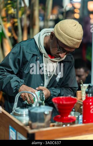 Nahaufnahme eines Straßencafés, der gekonnt Milch in eine Tasse frisch gebrühten Kaffee gießt. Eine häufige Szene auf südostasiatischen Straßenmärkten. Stockfoto