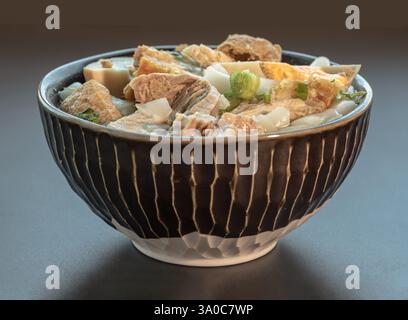 Gerollte Reisnudeln in fünf-Gewürzen-Brühe sind gekochte Eier, knuspriges Schweinefleisch, Schweinefleisch und Tofu in braun gedünsteter Suppe, serviert auf einer Keramikschale. Chinesisch Stockfoto