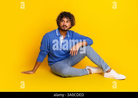 Porträt eines jungen gutaussehenden Mannes in lässiger Kleidung vor einem leuchtend gelben Hintergrund, der ein entspanntes und stilvolles Auftreten zeigt. Stockfoto