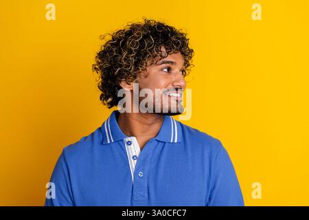 Porträt eines jungen Mannes mit lockigem Haar, der ein blaues Poloshirt vor einem leuchtend gelben Hintergrund trägt, in einer legeren und stilvollen Pose Stockfoto