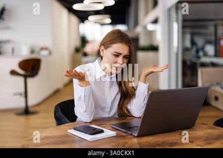 Junge Frau, die am Laptop arbeitet, hat Kopfschmerzen. Gelangweilte, arbeitaholische Buchhalterin mit Kopfschmerzen und Stress. Geschäftsfrau mit Migräne Stockfoto
