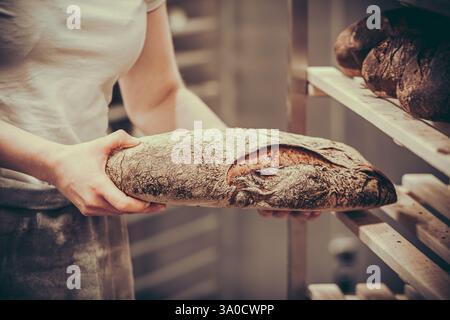 Bäckerin legt frisch gebackenes Brot auf ein Holzregal Stockfoto