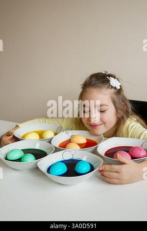 Ein lächelndes Mädchen bewundert ihre frisch gefärbten Ostereier in leuchtenden Farben Stockfoto