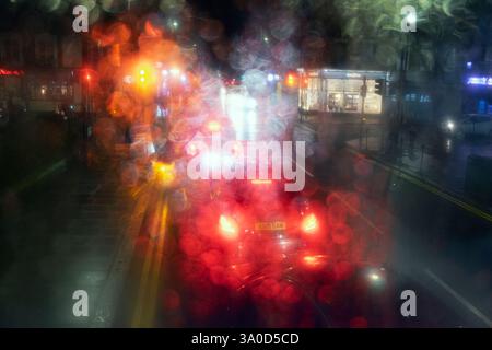 Blick auf farbenfrohe Geschäfte und Verkehrsampeln auf einer Straße bei Nacht in London Blick durch einen Doppeldeckerbus im obersten Stockwerk regnerisches Fenster London UK Stockfoto