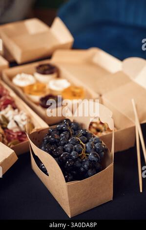 Aus nächster Nähe sehen Sie Heidelbeeren, süße Desserts und Fleisch, das auf dem Tisch in den Öko-Kisten aus Papier liegt. Stockfoto