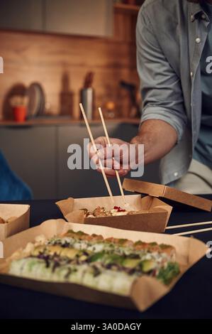 Mit Stäbchen. Ein Mann in legeren Kleidern hat Sushi, das in der Öko-Kiste aus Papier ist. Stockfoto