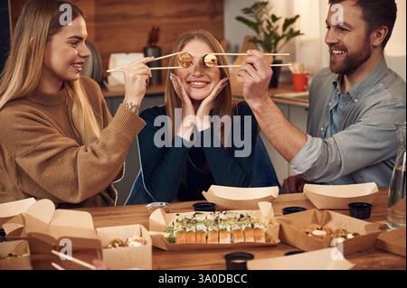 Spaß haben, Rollen des Essens vor den Augen der Frau. Freunde sitzen zuhause drinnen und essen zusammen Sushi. Stockfoto