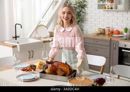 Schöne junge Frau mit leckerem gebackenem truthahn am Tisch in der Küche. Thanksgiving-Feiertag Stockfoto