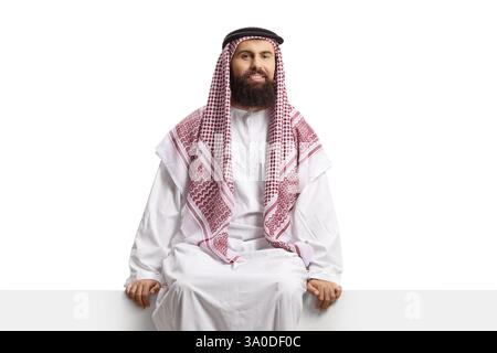 Saudi-arabischer Mann, der auf einer Tafel sitzt und die Kamera isoliert auf weißem Hintergrund betrachtet Stockfoto