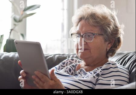 Ältere Frau auf Couch zu Hause mit schnurlosem Tablet Stockfoto