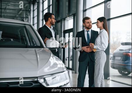 Der Mann berät ein junges Paar im Autohaus. Stockfoto