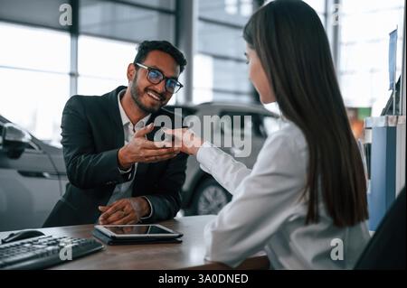 Frau berät den Mann im Autohaus. Ich nehme die Schlüssel aus dem neuen Auto. Stockfoto