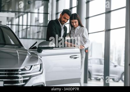 Mann in formeller Kleidung berät Frau über das Auto im Autohaus. Stockfoto
