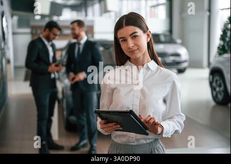Frau steht vor ihren Kollegen. Drei Personen arbeiten im Ausstellungsraum zusammen. Stockfoto