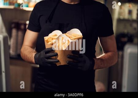 Der Mann steht und hält Pommes Frites in den Öko-Kisten aus Papier. Stockfoto