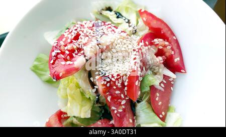Frisch zubereiteter Sesamsalat mit lebhaften Tomaten und knusprigem Salat, garniert mit gerösteten Sesamsamen, perfekt für eine gesunde Mittagszeit Stockfoto