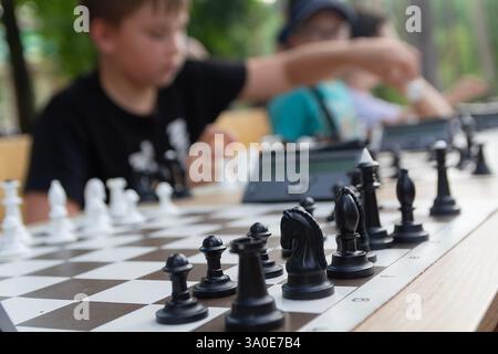 Die Hand eines Kindes bewegt sich während eines Schachturniers. Mehrere Schachtische hintereinander, Kinderturnier. Schachfiguren auf einem Schachbrett. Stockfoto