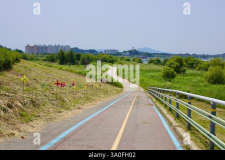 Buyeo County, Südkorea - 27. Mai 2021: Ein gewundener Radweg mit bunten Rädern führt in Richtung Buyeo City, mit üppigem Grün, weit entfernt Stockfoto
