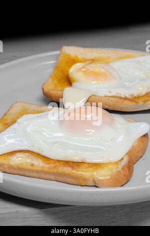 Spiegelei auf Toast auf einem grauen Steingut-Teller mit Holzbrett Hintergrund. Traditionelles Frühstücksessen. Stockfoto